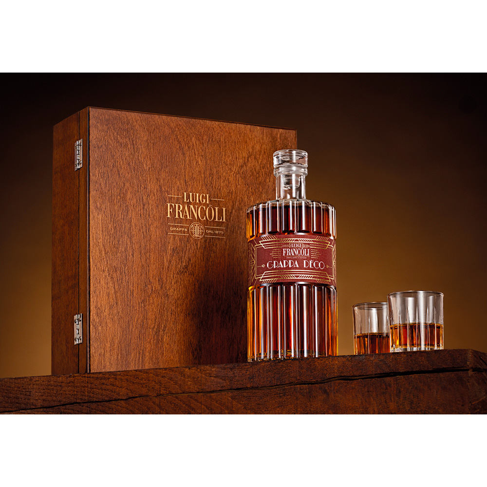 Francoli Grappa Riserva Decò: un elegante cassetta regalo in legno racchiude due bicchieri da degustazione per distillati e una bottiglia di grappa invecchiata Luigi Francoli Decò. Un vero e proprio tributo all'arte e all'eleganza dell'epoca Art Decò, avvolto nell'atmosfera inebriante dell'invecchiamento nel legno. Questa magnifica confezione regalo è l'occasione perfetta per trascorrere momenti estremamente piacevoli e conviviali. Luigi Francoli Grappa Riserva Decò: Si presenta di un bel colore ambrato, limpido e luminoso. Al naso giungono intense sensazioni di mandorla e nocciola tostata, a cui si susseguono sensazioni speziate di vaniglia, uva passa e frutta candita. Al palato è estremanente equilibrata, ricca e complessa. Il sorso è avvolgente e rotondo, il ritorno di note vanigliate e accenni di legno è notevole. Chiude con un finale di ottima persistenza gustativa.
