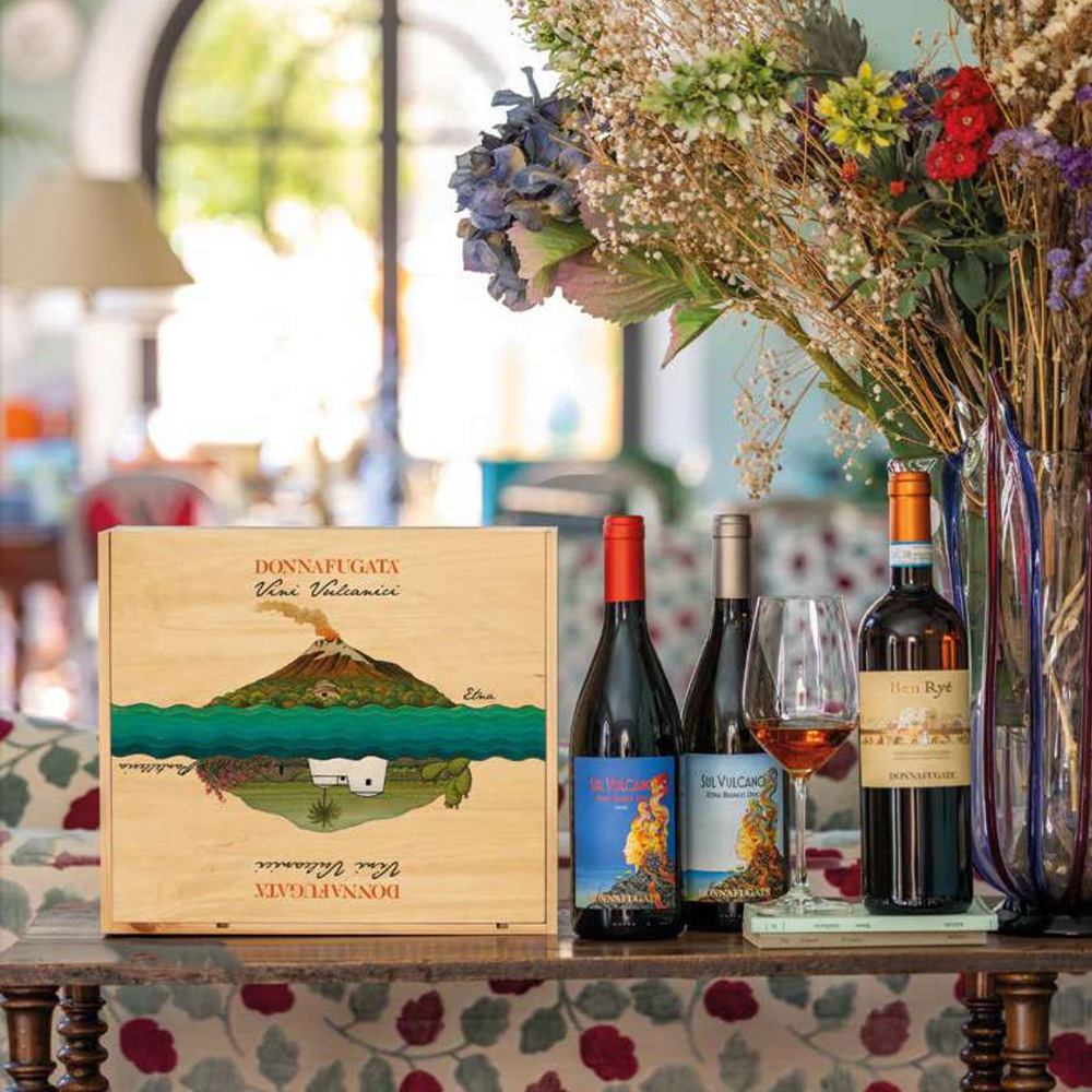 Donnafugata presenta la nuovissima e bellissima cassetta regalo che celebra i Vini Vulcanici più rappresentativi della Tenuta: Sul Vulcano Etna DOC Bianco 2021, Sul Vulcano Etna DOC Rosso 2021 e Ben Ryé Passito di Pantelleria DOC 2022. Tutti e tre vini che portano nel calice l'energia, la mineralità e l'eleganza dei loro territori di origine, ovvero l'isola di Pantelleria e l'Etna. Una bellissima confezione regalo con tre bottiglie, ideale per gli appassionati ed intenditori di vini, nonché della vivacità siciliana. - Sul Vulcano Etna DOC Bianco (Carricante 100%) Un bianco ricercato e ricco, che richiama i sentori di frutti gialli, erbe aromatiche, agrumi e sbuffi minerali di pietra focaia. Avvolgente, fresco e sapido al palato, caratterizzato dalla sua spiccata mineralità e dalla lunghissima persistenza. - Sul Vulcano Etna DOC Rosso (Nerello Mascalese e Nerello Cappuccio) Un rosso luminoso, con bouquet elegante che spazia dai sentori iniziali di ribes e fragolina, completati da gradevoli note floreali, seguite da spezie come cannella e noce moscata. Al palato rivela un tannino equilibrato e ben integrato, dimostrandosi un rosso armonico, dalla bellissima persistenza. - Ben Ryé Passito di Pantelleria DOC (100% Moscato d'Alessandria)Da sempre considerato "il Passito di Pantelleria", uno dei più grandi e meravigliosi vini da meditazione italiani. Si distingue per le caratteristiche note di albicocca e pesca, canditi e fichi secchi, seguiti ancora da miele, erbe aromatiche e note minerali. Morbido, intenso e piacevolmente ampio, si differenzia per la sua straordinaria complessità, fondendo in un unico nettare dolcezza, sapidità e morbidezza. Lunghissimo il finale. 