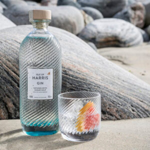 Isle of Harris Gin nasce sull’omonima isola al largo delle coste nord-occidentali della Scozia, nelle selvagge Ebridi Esterne. È un gin artigianale che incarna il carattere marino e autentico del territorio da cui proviene: ventoso, puro, essenziale. Il suo profilo racconta il respiro dell’oceano e i paesaggi incontaminati dell’isola, grazie a una botanica distintiva, l’alga Sugar Kelp, raccolta nei fondali marini locali. Il progetto nasce dal desiderio di Anderson Bakewell di catturare la bellezza e le atmosfere uniche dell’isola in un distillato. La distilleria è stata fondata nel 2015 nel villaggio costiero di Tarbert, e la produzione avviene in piccoli lotti, con un alambicco in rame e acqua purissima proveniente dalla sorgente di Abhainn Cnoc. La ricetta prevede nove botaniche, scelte con cura per esprimere freschezza, eleganza e territorialità: ginepro, scorze di agrumi, erbe, spezie e, soprattutto, Sugar Kelp, che dona al gin una caratteristica nota iodata e salina. Alla vista è cristallino e limpido. Al naso colpisce per la sua eleganza aromatica: note balsamiche di ginepro, aghi di pino, scorza di lime e pompelmo, erbe officinali, pepe bianco e una netta impronta marina. Al palato è armonico e setoso, con una piacevole freschezza salina che accompagna un finale lungo, pulito e balsamico. La bottiglia è un capolavoro di design firmato dallo studio Stranger & Stranger: vetro lavorato con onde in rilievo che evocano il mare, tappo in sughero naturale e un’etichetta minimale, a sottolineare l’eleganza sobria del progetto.