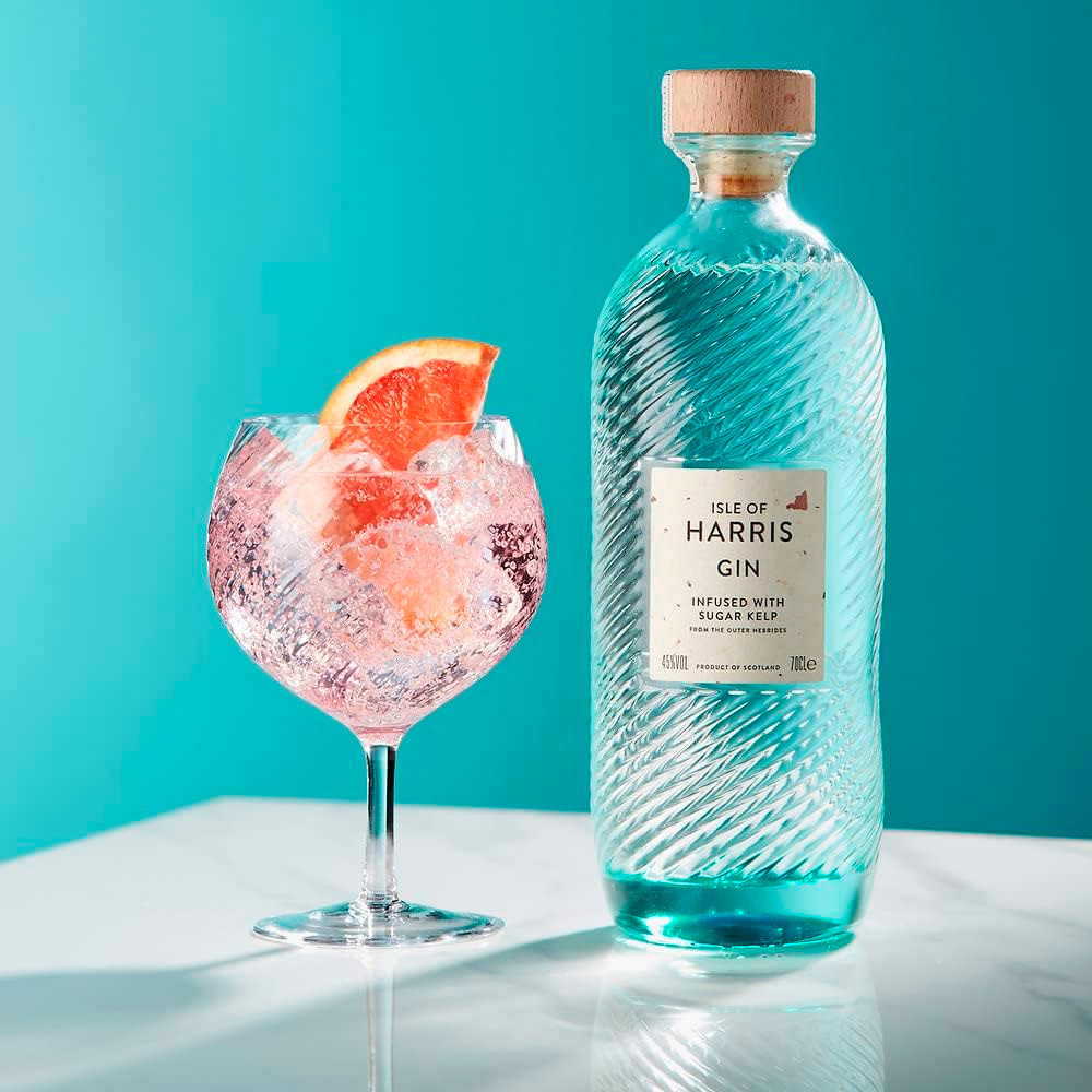 Isle of Harris Gin nasce sull’omonima isola al largo delle coste nord-occidentali della Scozia, nelle selvagge Ebridi Esterne. È un gin artigianale che incarna il carattere marino e autentico del territorio da cui proviene: ventoso, puro, essenziale. Il suo profilo racconta il respiro dell’oceano e i paesaggi incontaminati dell’isola, grazie a una botanica distintiva, l’alga Sugar Kelp, raccolta nei fondali marini locali. Il progetto nasce dal desiderio di Anderson Bakewell di catturare la bellezza e le atmosfere uniche dell’isola in un distillato. La distilleria è stata fondata nel 2015 nel villaggio costiero di Tarbert, e la produzione avviene in piccoli lotti, con un alambicco in rame e acqua purissima proveniente dalla sorgente di Abhainn Cnoc. La ricetta prevede nove botaniche, scelte con cura per esprimere freschezza, eleganza e territorialità: ginepro, scorze di agrumi, erbe, spezie e, soprattutto, Sugar Kelp, che dona al gin una caratteristica nota iodata e salina. Alla vista è cristallino e limpido. Al naso colpisce per la sua eleganza aromatica: note balsamiche di ginepro, aghi di pino, scorza di lime e pompelmo, erbe officinali, pepe bianco e una netta impronta marina. Al palato è armonico e setoso, con una piacevole freschezza salina che accompagna un finale lungo, pulito e balsamico. La bottiglia è un capolavoro di design firmato dallo studio Stranger & Stranger: vetro lavorato con onde in rilievo che evocano il mare, tappo in sughero naturale e un’etichetta minimale, a sottolineare l’eleganza sobria del progetto.