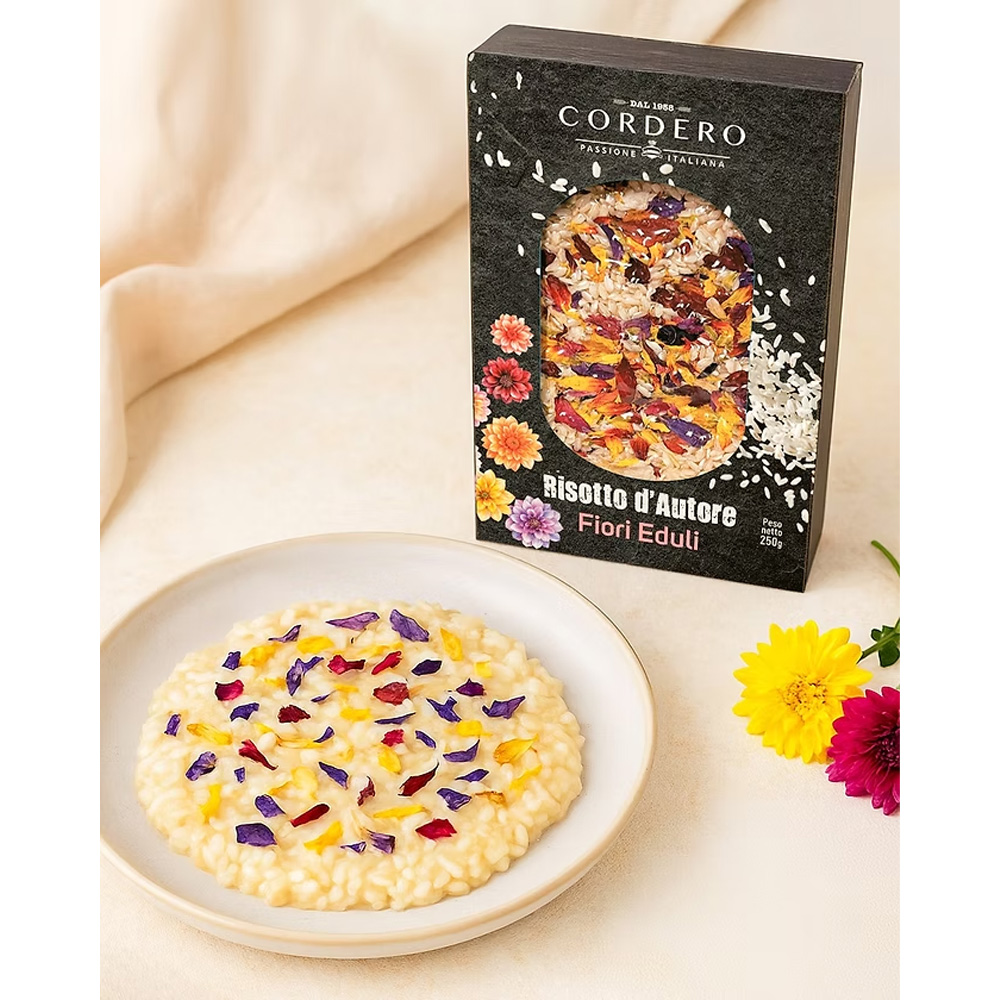 Il Risotto d’Autore Cordero ai Fiori Eduli è un piatto elegante e raffinato che unisce la qualità del riso Carnaroli al fascino dei petali colorati di fiori commestibili. Un mix unico che trasforma ogni preparazione in un’esperienza visiva e gustativa sorprendente. Realizzato con ingredienti selezionati, il risotto acquista profumi delicati e note floreali che lo rendono perfetto per stupire a tavola con un piatto tanto buono quanto scenografico. La confezione, curata come un piccolo quadro, presenta il riso disposto come un candido fondale impreziosito dai fiori variopinti: un invito a cucinare con creatività e stile.
