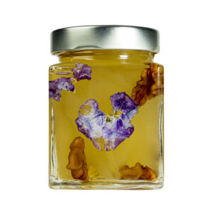 La Mostarda Pere, Noci e Viole del Pensiero è una variante innovativa, grazie al tocco distintivo delle viole del pensiero. Queste ultime conferiscono alla mostarda un tocco floreale intrigante e particolare, oltre che un tocco estetico di prestigio. Una composizione di sapori e consistenze unici: le pere mature sono dolci e succose, le noci donano croccantezza, il tutto completato dalle note floreali e colorate delle viole del pensiero. Si adatta particolarmente all'abbinamento con i formaggi stagionati o carni, ma è ottima anche gustata da sola. Grado di piccantezza generale: 9. Per le mostarde di frutta di Fredo vengono utilizzate solo le migliori materie prime di origine italiana.  Fredo vanta una lunga storia di produzione artigianale di mostarda e frutta candita, iniziata nel lontano 1890 a Brissago (Canton Ticino). Prodotta in esclusiva per EnoArt Enoteca da Fredo SA nel laboratorio di Cadenazzo (Svizzera). Prodotto artigianale, lavorato e confezionato a mano.Formato: Vasetto 400g