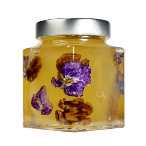 La Mostarda Pere, Noci e Viole del Pensiero è una variante innovativa, grazie al tocco distintivo delle viole del pensiero. Queste ultime conferiscono alla mostarda un tocco floreale intrigante e particolare, oltre che un tocco estetico di prestigio. Una composizione di sapori e consistenze unici: le pere mature sono dolci e succose, le noci donano croccantezza, il tutto completato dalle note floreali e colorate delle viole del pensiero. Si adatta particolarmente all'abbinamento con i formaggi stagionati o carni, ma è ottima anche gustata da sola. Grado di piccantezza generale: 9. Per le mostarde di frutta di Fredo vengono utilizzate solo le migliori materie prime di origine italiana.  Fredo vanta una lunga storia di produzione artigianale di mostarda e frutta candita, iniziata nel lontano 1890 a Brissago (Canton Ticino). Prodotta in esclusiva per EnoArt Enoteca da Fredo SA nel laboratorio di Cadenazzo (Svizzera). Prodotto artigianale, lavorato e confezionato a mano.Formato: Vasetto 400g