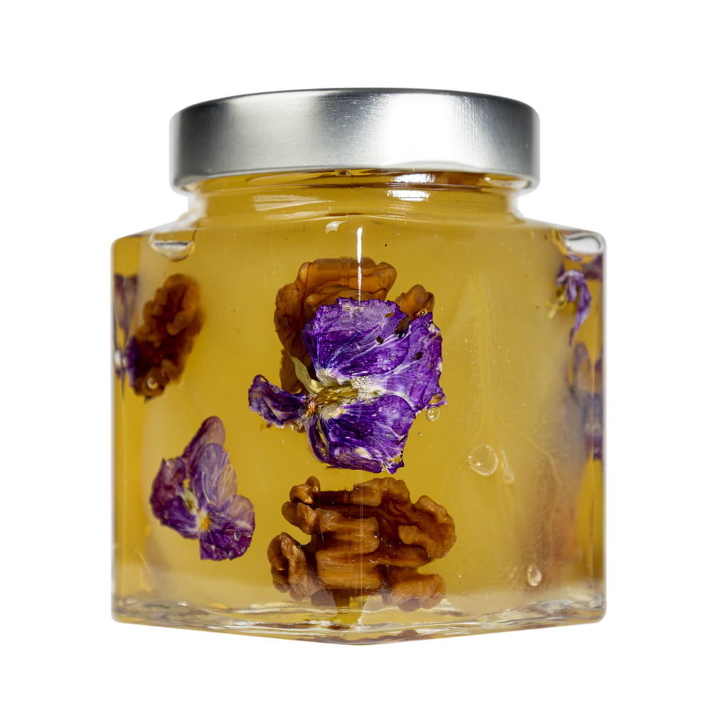 La Mostarda Pere, Noci e Viole del Pensiero è una variante innovativa, grazie al tocco distintivo delle viole del pensiero. Queste ultime conferiscono alla mostarda un tocco floreale intrigante e particolare, oltre che un tocco estetico di prestigio. Una composizione di sapori e consistenze unici: le pere mature sono dolci e succose, le noci donano croccantezza, il tutto completato dalle note floreali e colorate delle viole del pensiero. Si adatta particolarmente all'abbinamento con i formaggi stagionati o carni, ma è ottima anche gustata da sola. Grado di piccantezza generale: 9. Per le mostarde di frutta di Fredo vengono utilizzate solo le migliori materie prime di origine italiana.  Fredo vanta una lunga storia di produzione artigianale di mostarda e frutta candita, iniziata nel lontano 1890 a Brissago (Canton Ticino). Prodotta in esclusiva per EnoArt Enoteca da Fredo SA nel laboratorio di Cadenazzo (Svizzera). Prodotto artigianale, lavorato e confezionato a mano.Formato: Vasetto 400g