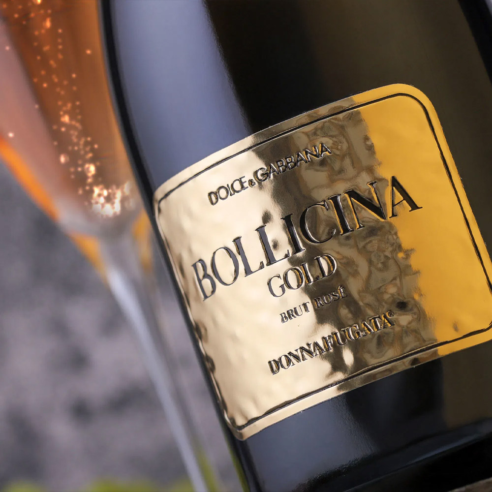 Donnafugata Dolce&Gabbana Bollicina Gold Spumante Brut Rosé Sicilia DOC si presenta con un elegante colore rosa antico dai riflessi dorati. Al naso offre un bouquet fine e complesso, con note di crosta di pane tipiche della rifermentazione in bottiglia, accompagnate da sentori fruttati di agrumi, ribes rosso e pompelmo rosa. Al palato è fresco e vibrante, con una marcata mineralità vulcanica e una bollicina fine e persistente. L’equilibrio tra acidità e morbidezza conduce a un finale lungo, sapido, di grande eleganza e precisione aromatica. Bollicina Gold nasce da uve Nerello Mascalese in purezza, coltivate in vigneti posti alle pendici dell’Etna, nel comune di Randazzo. I terreni di origine vulcanica e le forti escursioni termiche favoriscono una maturazione lenta e regolare, esaltando la freschezza e la complessità aromatica. L’annata 2019 è stata fresca, con piogge ben distribuite che hanno contribuito a un profilo aromatico intenso e definito. Uno spumante rosé di rara finezza, capace di evolvere armoniosamente fino a 8-10 anni. Questa edizione “Gold” nasce dal dialogo tra Dolce&Gabbana e Donnafugata: una celebrazione della creatività e dell’artigianalità italiana. Il packaging, prezioso e scenografico, interpreta lo stile iconico di Dolce&Gabbana e rende Bollicina Gold un vino perfetto per occasioni speciali e regali esclusivi.