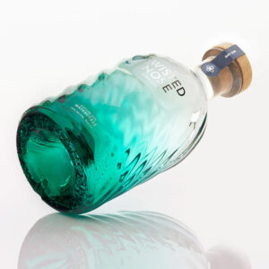 Twisted Nose Gin è un gin secco pluripremiato prodotto nell’Hampshire, pensato per racchiudere la purezza e la freschezza dei corsi d’acqua calcarei (chalk streams) che scorrono vicino alla distilleria. Realizzato in piccoli lotti e distillato lentamente in alambicchi di rame, nasce per valorizzare la provenienza e il legame con un habitat naturale unico. La firma aromatica è il crescione fresco locale, naturalmente pepato, che dà al distillato un tocco stimolante e un finale vivace e persistente; il riferimento storico richiama il nome romano “Nasturtium”, interpretato come “naso storto”. Accanto al ginepro, una selezione di botaniche completa il profilo con equilibrio: pompelmo, corteccia di cassia, semi di finocchio, iris, radice di angelica, lavanda, agrumi e coriandolo, distillate con cura per mantenerne gli aromi freschi e delicati. Al naso risulta morbido, con sfumature erbacee e un accenno speziato; al palato è fresco, secco e ben bilanciato, con note di pompelmo e finocchio, cenni delicatamente floreali e una chiusura pepata distintiva legata al crescione. La persistenza è lunga e pulita, con una sensazione complessiva intensa ma mai pesante. Anche il design è parte dell’esperienza: la bottiglia personalizzata in vetro blu-verde presenta un effetto ondulato che increspa e rifrange la luce come la superficie di un ruscello, anticipando visivamente la sua anima “di fiume”. In servizio è ideale in Gin Tonic con una fetta di pompelmo rosa per esaltare la componente agrumata, ed è eccellente anche in Martini con vermouth, dove la sua secchezza e la traccia erbacea emergono con grande precisione.