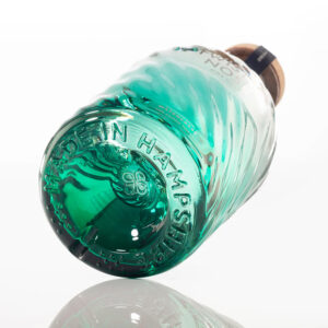 Twisted Nose Gin è un gin secco pluripremiato prodotto nell’Hampshire, pensato per racchiudere la purezza e la freschezza dei corsi d’acqua calcarei (chalk streams) che scorrono vicino alla distilleria. Realizzato in piccoli lotti e distillato lentamente in alambicchi di rame, nasce per valorizzare la provenienza e il legame con un habitat naturale unico. La firma aromatica è il crescione fresco locale, naturalmente pepato, che dà al distillato un tocco stimolante e un finale vivace e persistente; il riferimento storico richiama il nome romano “Nasturtium”, interpretato come “naso storto”. Accanto al ginepro, una selezione di botaniche completa il profilo con equilibrio: pompelmo, corteccia di cassia, semi di finocchio, iris, radice di angelica, lavanda, agrumi e coriandolo, distillate con cura per mantenerne gli aromi freschi e delicati. Al naso risulta morbido, con sfumature erbacee e un accenno speziato; al palato è fresco, secco e ben bilanciato, con note di pompelmo e finocchio, cenni delicatamente floreali e una chiusura pepata distintiva legata al crescione. La persistenza è lunga e pulita, con una sensazione complessiva intensa ma mai pesante. Anche il design è parte dell’esperienza: la bottiglia personalizzata in vetro blu-verde presenta un effetto ondulato che increspa e rifrange la luce come la superficie di un ruscello, anticipando visivamente la sua anima “di fiume”. In servizio è ideale in Gin Tonic con una fetta di pompelmo rosa per esaltare la componente agrumata, ed è eccellente anche in Martini con vermouth, dove la sua secchezza e la traccia erbacea emergono con grande precisione.