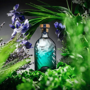 Twisted Nose Gin è un gin secco pluripremiato prodotto nell’Hampshire, pensato per racchiudere la purezza e la freschezza dei corsi d’acqua calcarei (chalk streams) che scorrono vicino alla distilleria. Realizzato in piccoli lotti e distillato lentamente in alambicchi di rame, nasce per valorizzare la provenienza e il legame con un habitat naturale unico. La firma aromatica è il crescione fresco locale, naturalmente pepato, che dà al distillato un tocco stimolante e un finale vivace e persistente; il riferimento storico richiama il nome romano “Nasturtium”, interpretato come “naso storto”. Accanto al ginepro, una selezione di botaniche completa il profilo con equilibrio: pompelmo, corteccia di cassia, semi di finocchio, iris, radice di angelica, lavanda, agrumi e coriandolo, distillate con cura per mantenerne gli aromi freschi e delicati. Al naso risulta morbido, con sfumature erbacee e un accenno speziato; al palato è fresco, secco e ben bilanciato, con note di pompelmo e finocchio, cenni delicatamente floreali e una chiusura pepata distintiva legata al crescione. La persistenza è lunga e pulita, con una sensazione complessiva intensa ma mai pesante. Anche il design è parte dell’esperienza: la bottiglia personalizzata in vetro blu-verde presenta un effetto ondulato che increspa e rifrange la luce come la superficie di un ruscello, anticipando visivamente la sua anima “di fiume”. In servizio è ideale in Gin Tonic con una fetta di pompelmo rosa per esaltare la componente agrumata, ed è eccellente anche in Martini con vermouth, dove la sua secchezza e la traccia erbacea emergono con grande precisione.